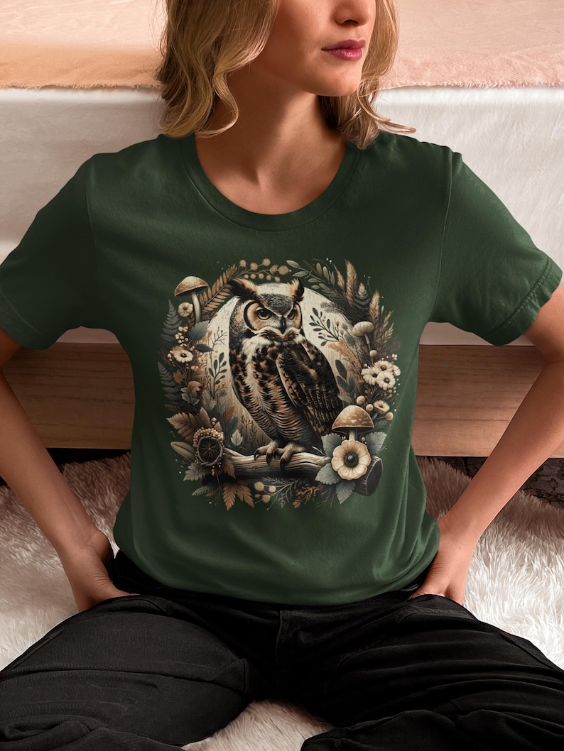 May include: A green t-shirt featuring an illustration of a brown and white owl surrounded by mushrooms and leaves.