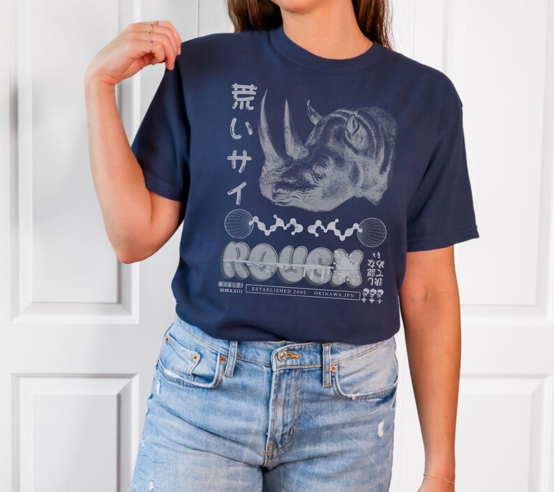 May include: A navy blue t-shirt with a white graphic of a rhinoceros and the text "ROUGH" in a stylized font. The text "ESTABLISHED 1963 OKINAWA, JPN" is also printed on the shirt.