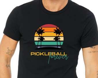 May include: A black t-shirt featuring a retro sunset graphic with palm trees and the text "Pickleball forever" in teal.