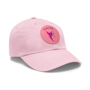 May include: Pink baseball cap with a round, pink patch featuring a purple fairy silhouette and the text "Dinker Bell".