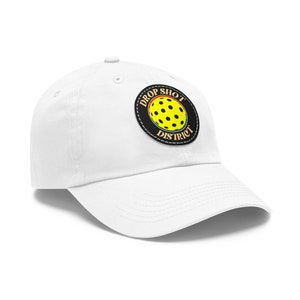 Può includere: Cappellino da baseball bianco con una toppa nera e gialla che dice "Drop Shot District" con una palla da pickleball all'interno del cerchio.