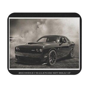 May include: Black and white image of a 2016 Dodge Challenger SRT Hellcat. The car is black and appears to be parked on a gravel surface. The image has a vintage feel with smoke in the background. The text "2016 Dodge Challenger SRT Hellcat" is at the bottom.