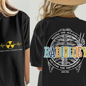 May include: Black t-shirt with a radiology theme. The front features a yellow radiation symbol and text. The back displays a skeleton graphic with the word "RADIOLOGY" and the phrase "Seeing the Invisible, Solving the Impossible."