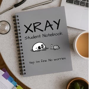 May include: A gray spiral-bound notebook with black text that reads XRAY Student Notebook and Yep. I'm fine. No worries. The cover features a black and white illustration of a skull partially submerged with a skeletal hand giving a thumbs up.