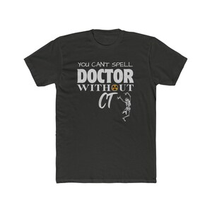 May include: Dark gray t-shirt with the text "YOU CAN'T SPELL DOCTOR WITHOUT CT" in white. A radiation symbol is above the word "UT". A skeleton graphic is below the text. The shirt is made of a soft, comfortable material.
