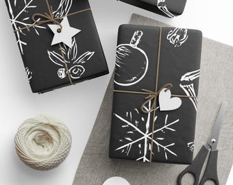 May include: Overhead shot of wrapped gifts with black paper and white holiday-themed illustrations. Each package is tied with twine and a white tag. A ball of twine, scissors, and blank tags are also visible.