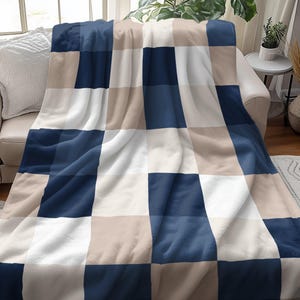 May include: A soft, plush throw blanket with a checkered pattern in shades of blue, beige, and white. The blanket is folded and draped over a couch.