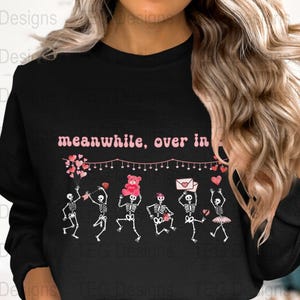 May include: Black sweatshirt with a pink graphic of skeletons dancing with hearts and the text "meanwhile, over in..."