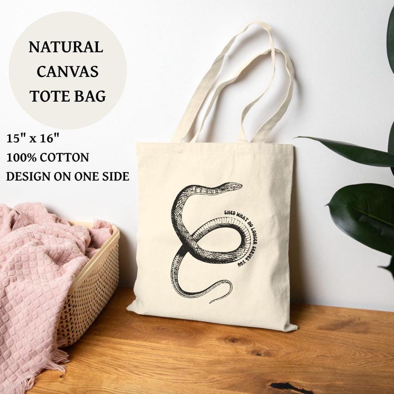 May include: A natural canvas tote bag, approximately 38cm x 41cm, featuring a black snake illustration and the text "Shed what no longer serves you." The bag is made of 100% cotton and has a design on one side.