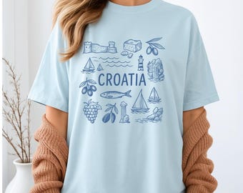 Op de afbeelding: Lichtblauw T-shirt met een Kroatië-ontwerp. Het ontwerp bevat illustraties van bezienswaardigheden, zeilboten en het woord "Croatia" in blauw. Het shirt heeft een relaxte pasvorm.