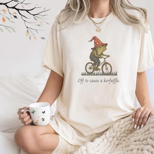 Camiseta de rana maga caprichosa, camiseta "Off to Cause a Kerfuffle", camiseta gráfica divertida surrealista cottagecore, camiseta con estética weirdcore de rana en bicicleta