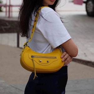 May include: A yellow leather shoulder bag with a silver zipper and a small tassel. The bag has a curved shape and a strap with metal accents.