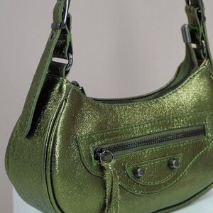May include: A green leather handbag with a short strap and a zippered pocket. The bag has a metallic sheen and a small tassel.