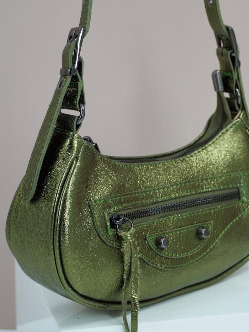 May include: A green leather handbag with a short strap and a zippered pocket. The bag has a metallic sheen and a small tassel.