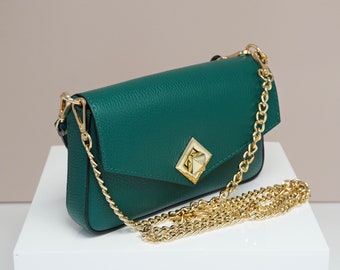 May include: A small, emerald green leather crossbody bag with a gold chain strap and a gold, geometric closure.