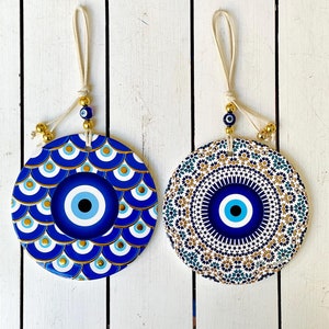 May include: Two round ceramic wall hangings featuring blue and gold evil eye designs. The evil eyes are surrounded by intricate patterns. Each hanging has a white string loop for hanging.