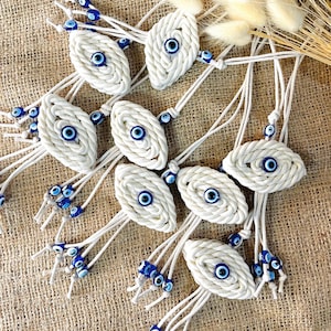 Peut inclure: Plusieurs breloques en forme d'œil de protection en corde blanche, ornées de perles bleues et blanches. Les breloques ovales présentent un motif d'œil bleu au centre. Chaque breloque est attachée à une ficelle blanche avec des perles supplémentaires.