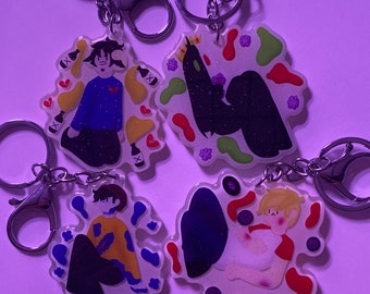 May include: Four colorful keychains featuring cartoon characters with different backgrounds. The keychains are made of clear acrylic with glitter embedded in the background. The characters are all in different poses and have different expressions.