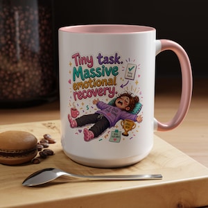 May include: White ceramic mug with a pink interior and handle. The mug features a colorful illustration with the text "Tiny task. Massive emotional recovery." A cartoon figure is lying down, with the words "I did the thing" on their shirt.