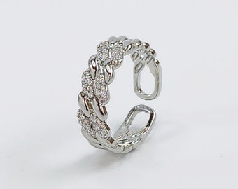 May include: A silver ring with a braided design and clear cubic zirconia stones.