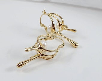 May include: A pair of gold hoop earrings with a delicate, organic design. Each earring features a small pearl nestled within the intricate metalwork.