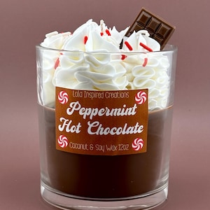 May include: A clear glass candle with a brown wax base, topped with white whipped wax, red sprinkles, and a chocolate square. The candle has a label that reads "Peppermint Hot Chocolate" and is made with coconut and soy wax.