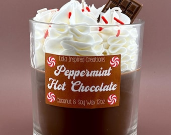 May include: A clear glass candle with a brown wax base, topped with white whipped wax, red sprinkles, and a chocolate square. The candle has a label that reads "Peppermint Hot Chocolate" and is made with coconut and soy wax.