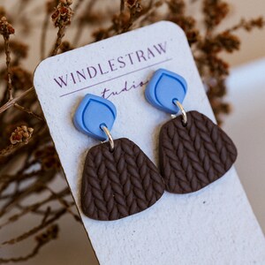 May include: A pair of brown and blue earrings with a knitted texture. The earrings are displayed on a white card with the text "Windlestraw Studio" and "Handmade in WA".