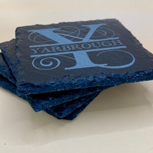 May include: Set of four slate coasters with a personalized design. The coasters are dark gray and feature a white engraved initial "Y" with the name "YARBROUGH" below it.