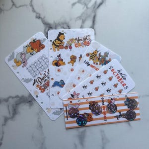 May include: A set of five white planner inserts featuring Winnie the Pooh characters in Halloween costumes. The sheets include various illustrations, small circular icons, and text such as "You got candy?", "Don't save", and "hello OCTOBER".