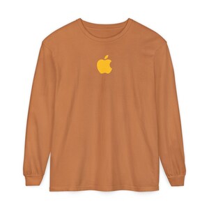 May include: A long-sleeved, crew neck shirt in a warm, earthy orange color. The shirt features a yellow apple logo centered on the chest. The sleeves are long and end at the wrists.