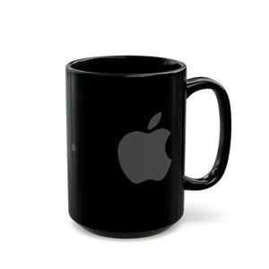 Könnte beinhalten: Schwarze Keramiktasse mit großem grauem Apple-Logo. Die Tasse hat einen gebogenen Henkel und eine glänzende Oberfläche. Geeignet für heiße oder kalte Getränke. Höhe ca. 10 cm.