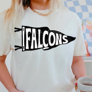 May include: White t-shirt with a black pennant design that says "FALCONS" in white letters.