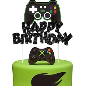 May include: Black and green cake topper with a video game controller and the words "Happy Birthday" in glitter.