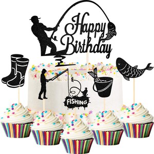 May include: Black and white cake toppers with a fishing theme. The toppers include a fishing rod, a bucket, a fish, and a pair of boots. The toppers are placed on top of cupcakes with colourful sprinkles.
