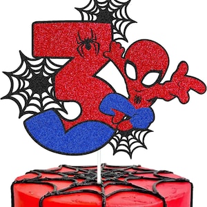 May include: Red and blue glitter cake topper featuring a cartoon Spiderman character with a black spider web design. The number 3 is incorporated into the design.