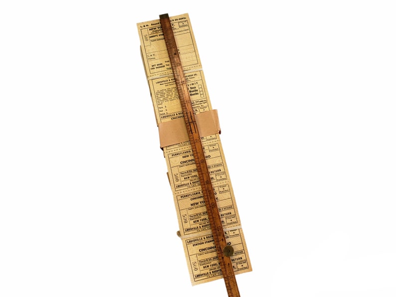 K&ouml;nnte beinhalten: Ein Stapel alter Zugtickets mit Zielen wie New York, Cincinnati und Louisville. Die Tickets sind mit einem braunen Papierband zusammengehalten und ein Holzliniall liegt daneben.