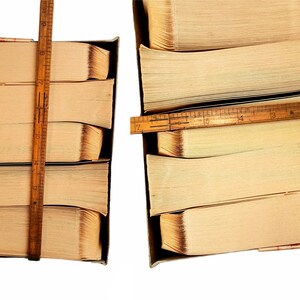 May include: Two stacks of old, yellowed books are bound together with wooden rulers. The stacks are in cardboard boxes. The books are about 12 inches tall.