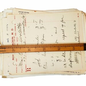May include: A stack of old medical prescription forms with handwritten notes and a ruler on top. The top form has the name "Roy" and a phone number. The bottom form has the name "Mackin, M.D." and a phone number.