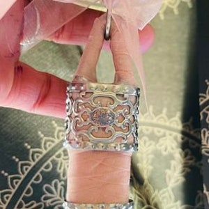 May include: A silver lighter with a decorative, ornate design. The lighter is attached to a pink ribbon and a pink rose quartz charm.