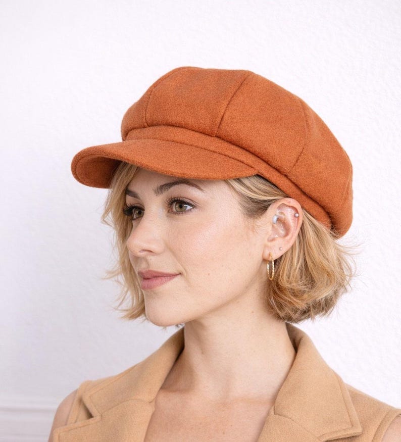 Side view of woman wearing a brown Baker Boy Cap and coat against a white background.