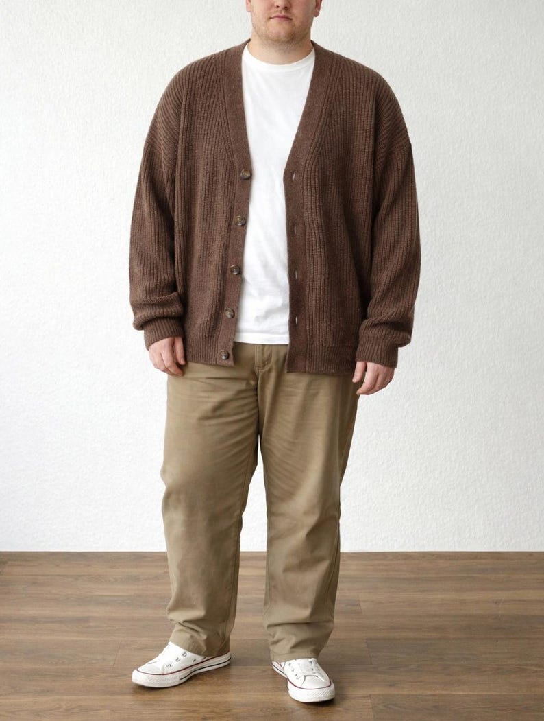 Person wearing a brown Plus Size Button Front Cardigan, white shirt, black pants, and blue sneakers against a light pink wall.