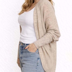 Side view of woman wearing a beige Batwing Sleeve Cardigan, white tank top, and blue jeans on a wooden floor.