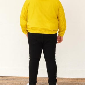Back view of person wearing a yellow Plus Size Mens Windbreaker Jacket and black pants standing against a white wall.