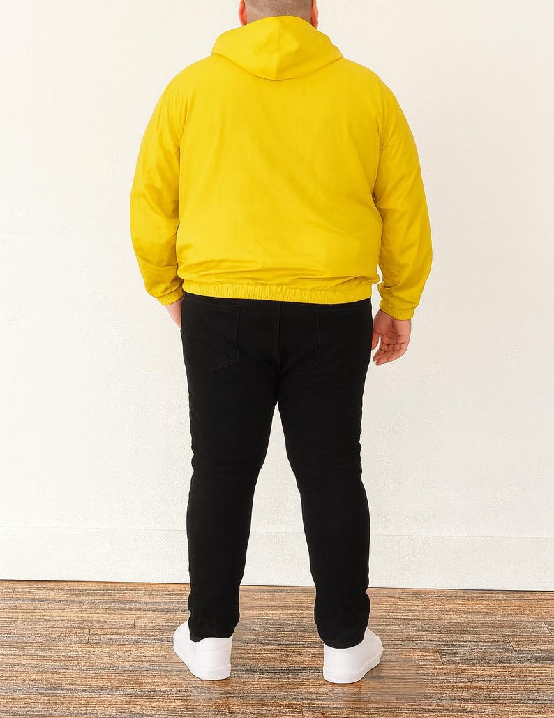 Back view of person wearing a yellow Plus Size Mens Windbreaker Jacket and black pants standing against a white wall.