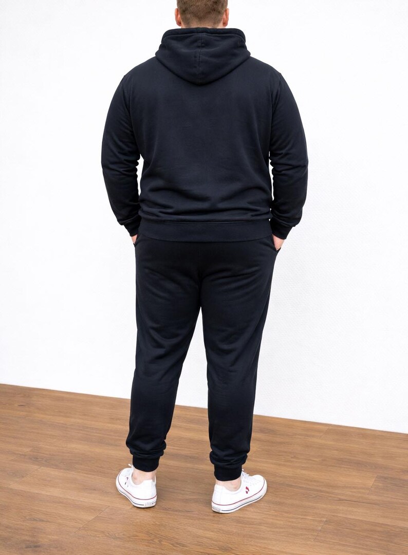 Back view of person wearing a black Plus Size Mens Classic Hoodie and pants with white sneakers on a wooden floor.