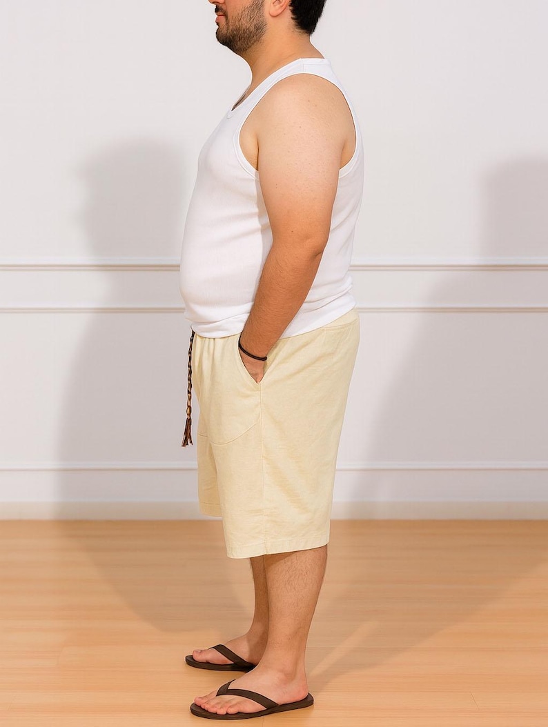 Side view of person wearing a white tank top and beige Plus Size Drawstring Knee Length Shorts standing against a plain white wall.