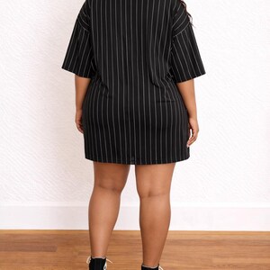 Back view of woman wearing a black pinstripe Plus Size T-Shirt Dress with black high-top sneakers on a wooden floor.