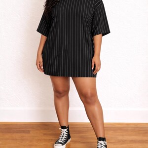 Woman wearing a black pinstripe Plus Size T-Shirt Dress with black high-top sneakers on a wooden floor.