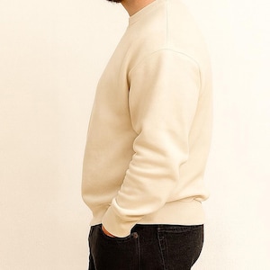 Side view of man wearing a beige sweater and black pants against a white background.